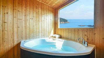 Una cabaña de madera con una bañera grande, una ventana con vistas al mar y una cesta con vasos.