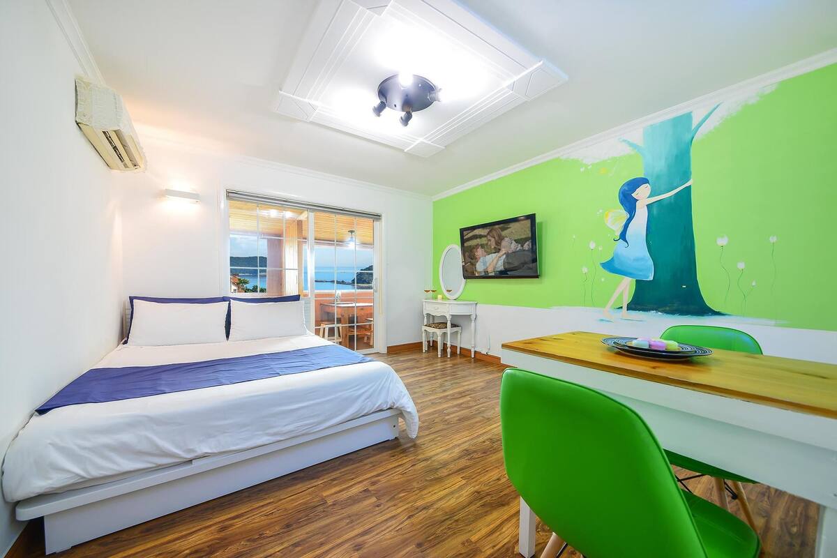 A modern hotel room with a bed, desk, and green chairs.