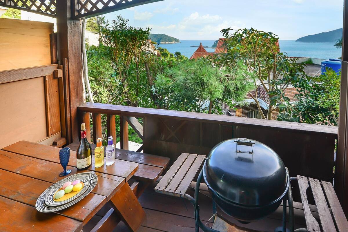 A wooden deck with a grill, bottles, and a plate of food.