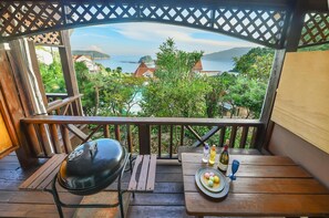 A wooden deck with a grill, a table with a bottle of wine, and a view of a coastal landscape. - Geoje Purenneoul Pension (Geoje)
