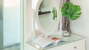 Un tocador de baño con superficie de vidrio, un mueble blanco, un espejo redondo y una planta en maceta.