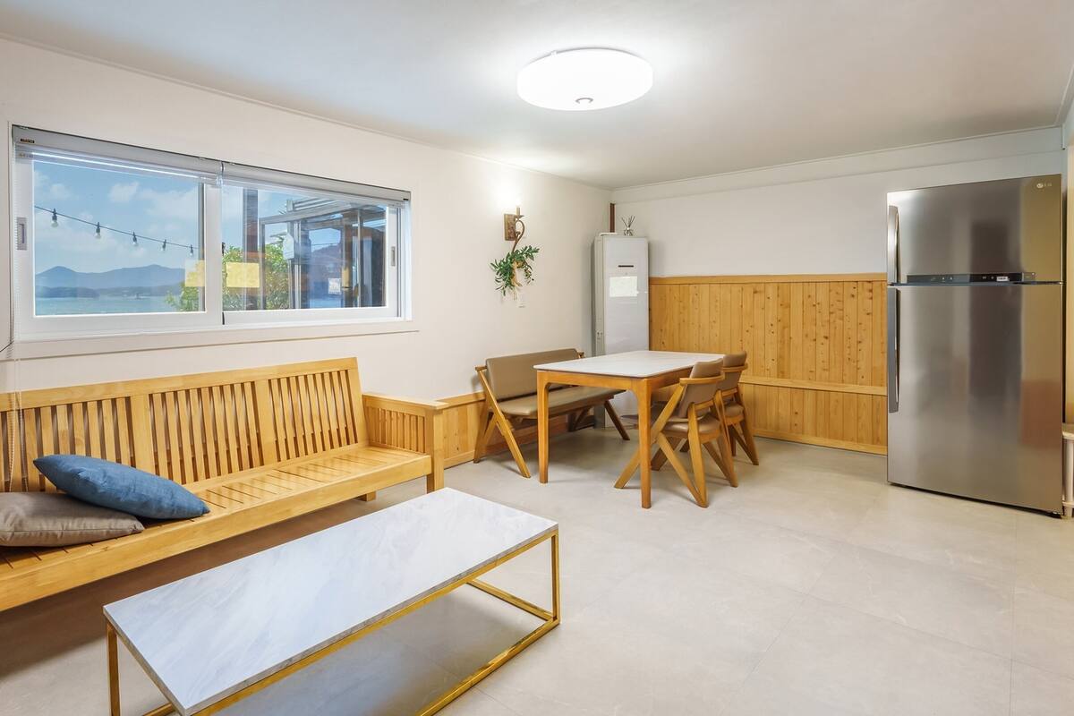 A modern kitchen with a wooden bench, a dining table, and a stainless steel refrigerator.