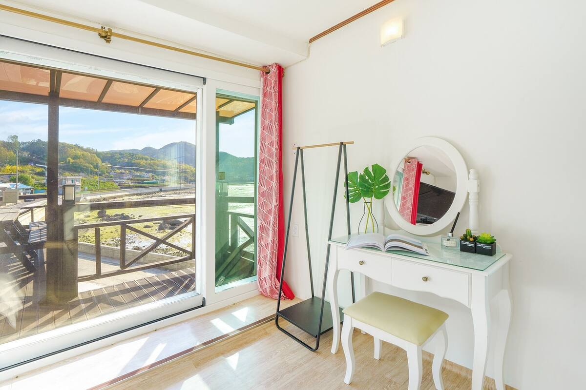 A room with a sliding glass door leading to a balcony with a view of a green landscape and mountains.
