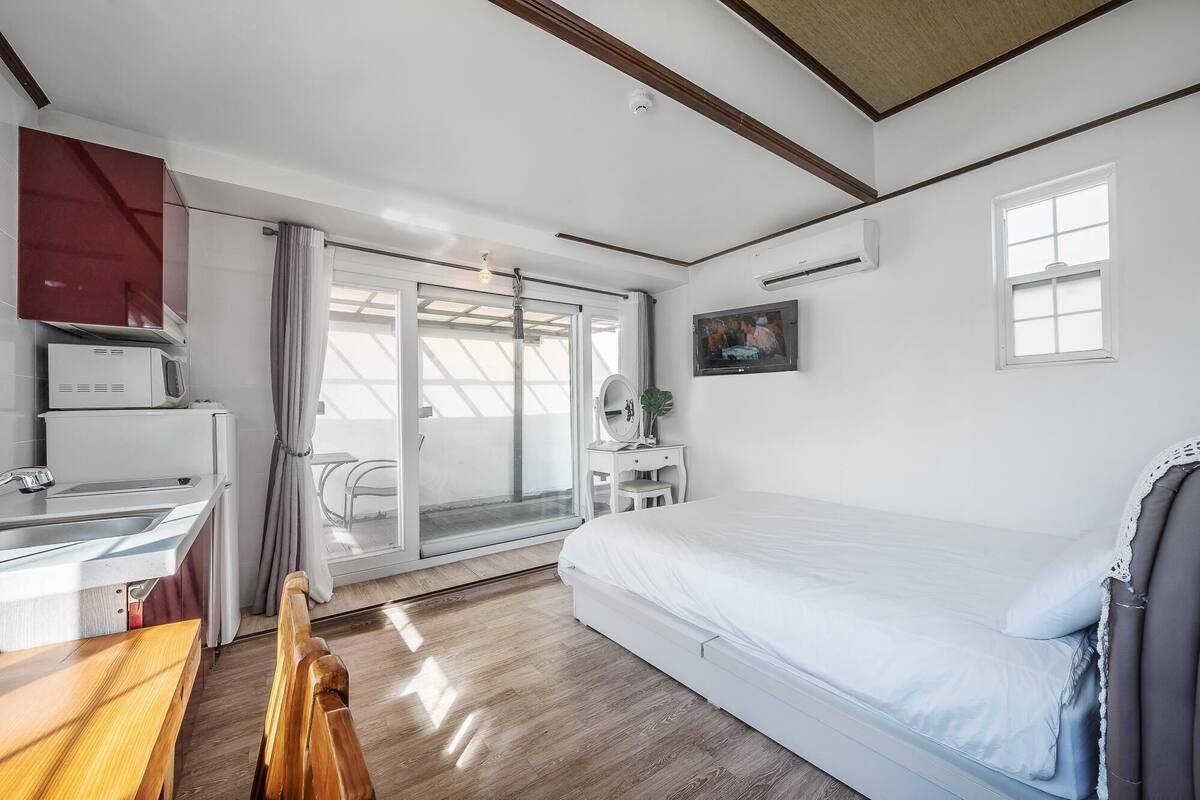 A hotel room with a bed, a desk with a sink, a microwave, a TV, and a sliding glass door to the balcony.