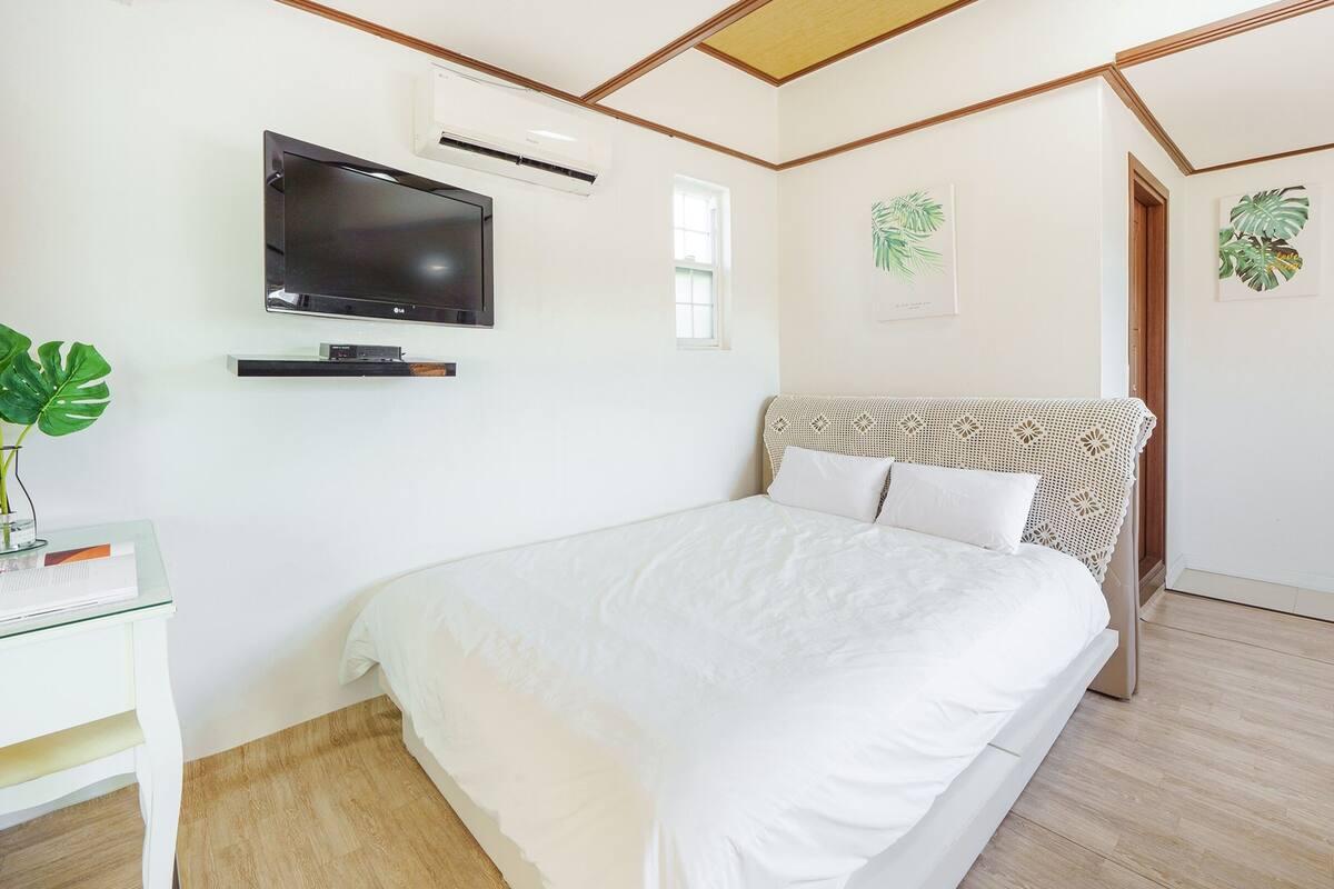 A bedroom with a bed, a TV mounted on the wall, and a window.