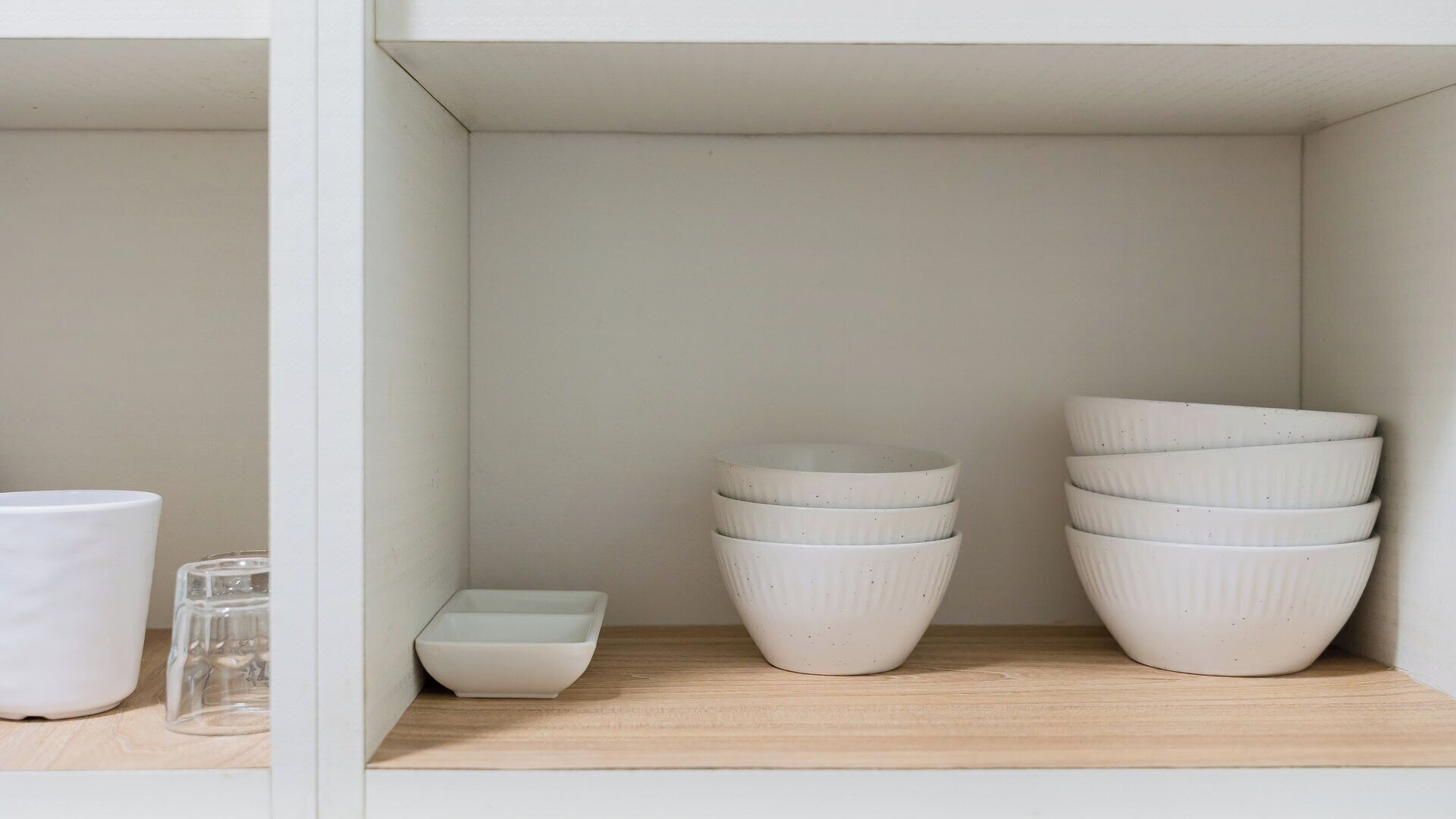 A shelf with various white ceramic containers and a glass.