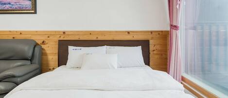 A hotel room with a wooden headboard, a grey leather sofa, a bed with white bedding, and a window with pink curtains.