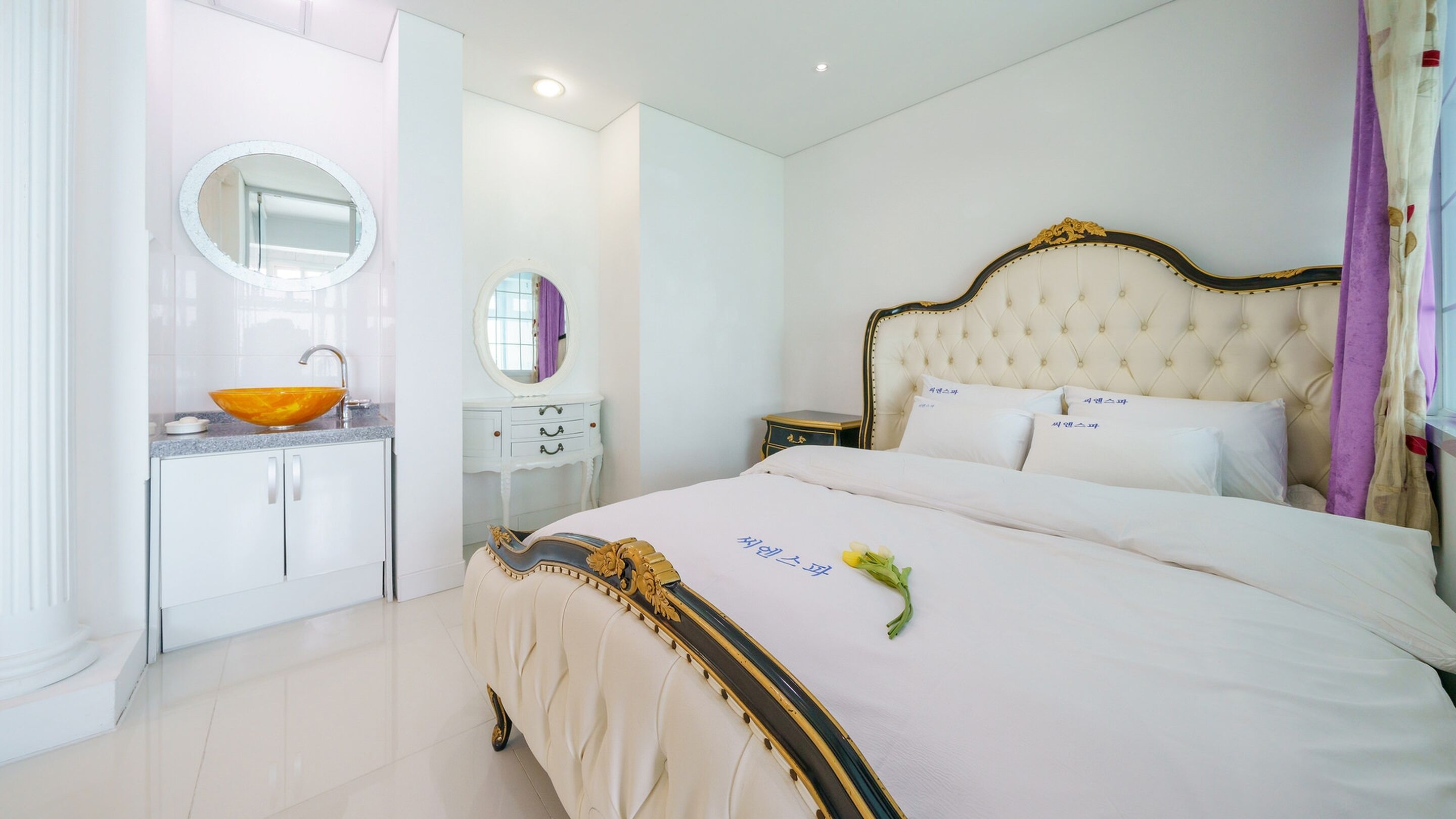 A bedroom with a bed, a vanity with a mirror, and a nightstand.