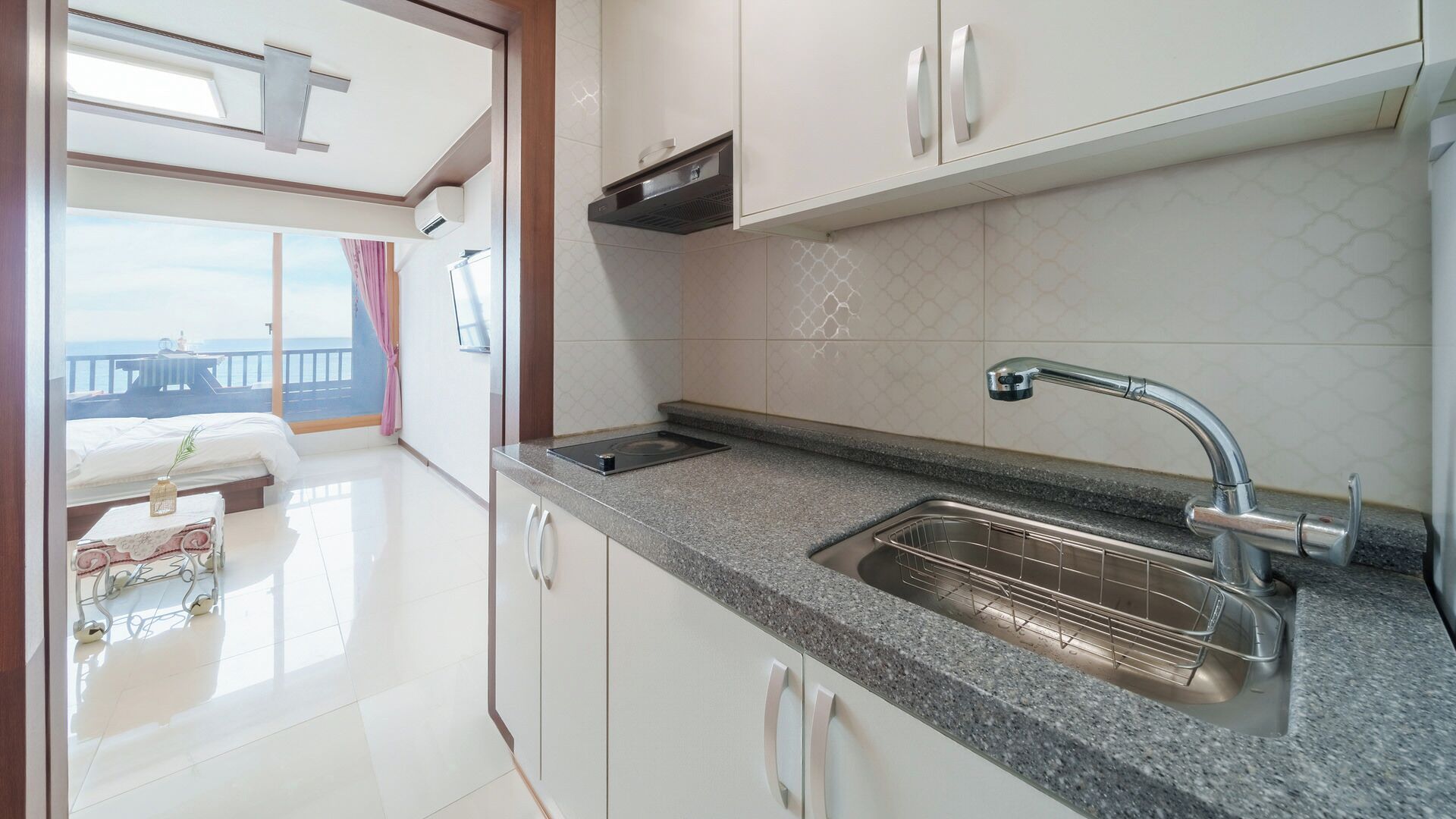 A modern kitchen with a granite countertop, stainless steel sink, and white cabinetry.