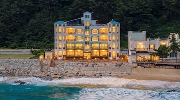 A multi-story hotel with balconies, located by a beach with waves.