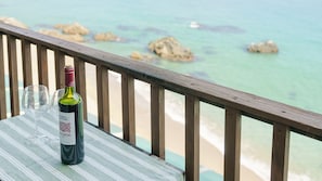 A bottle of wine and an empty glass on a table with a view of the ocean and rocks.