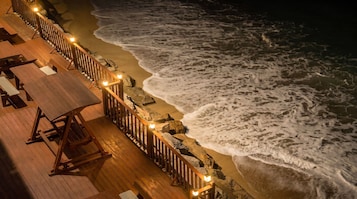 A wooden deck with tables and benches overlooking the ocean at night.