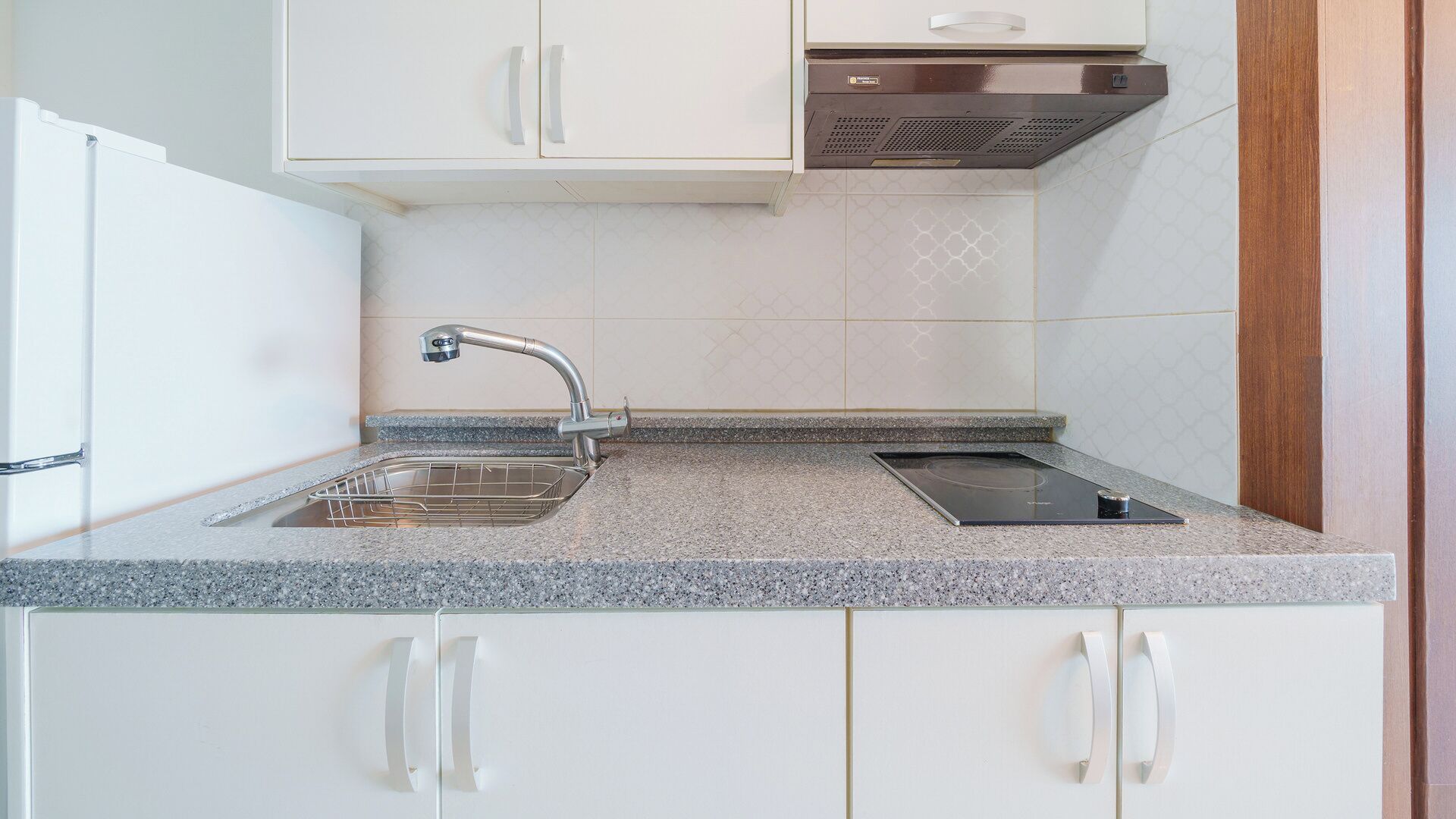 A kitchen with white cabinets, a stainless steel sink, and a built-in electric stove.