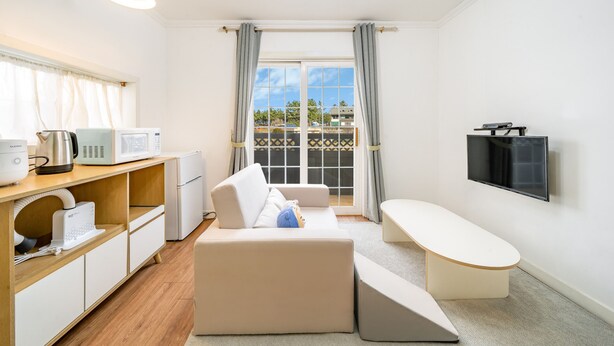 Un espacio habitable compacto con kitchenette, un sofá, un banco y un televisor montado en la pared.