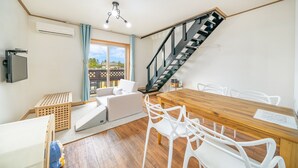 Una sala de estar moderna con una mesa de comedor de madera, sillas blancas, un sofá y una escalera.