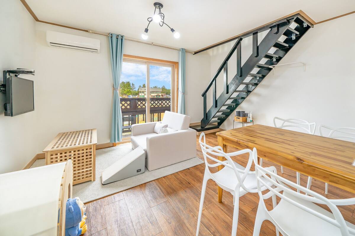 Un salon moderne avec une table à manger en bois, des chaises blanches, un canapé et un escalier.