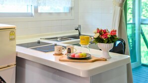 Et køkken med en hvid bordplade, kaffemaskine, kop, en tallerken med farverige kager og en vase med blomster.