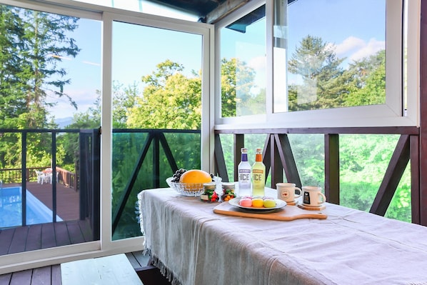 Une pièce baignée de lumière, avec une table mise pour le petit-déjeuner, agrémentée d’un panier de fruits, de bouteilles et de tasses.