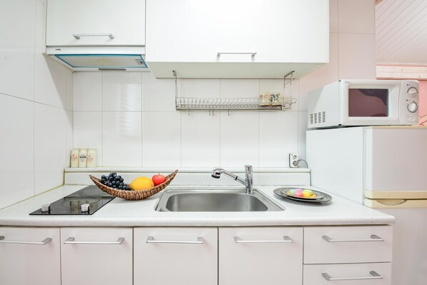 Cocina moderna con armarios blancos, un lavamanos de acero inoxidable, un microondas y una cesta de frutas.
