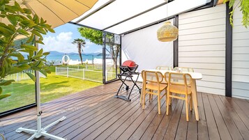 Una terraza de madera con mesa y sillas, una parrilla y vista al mar.