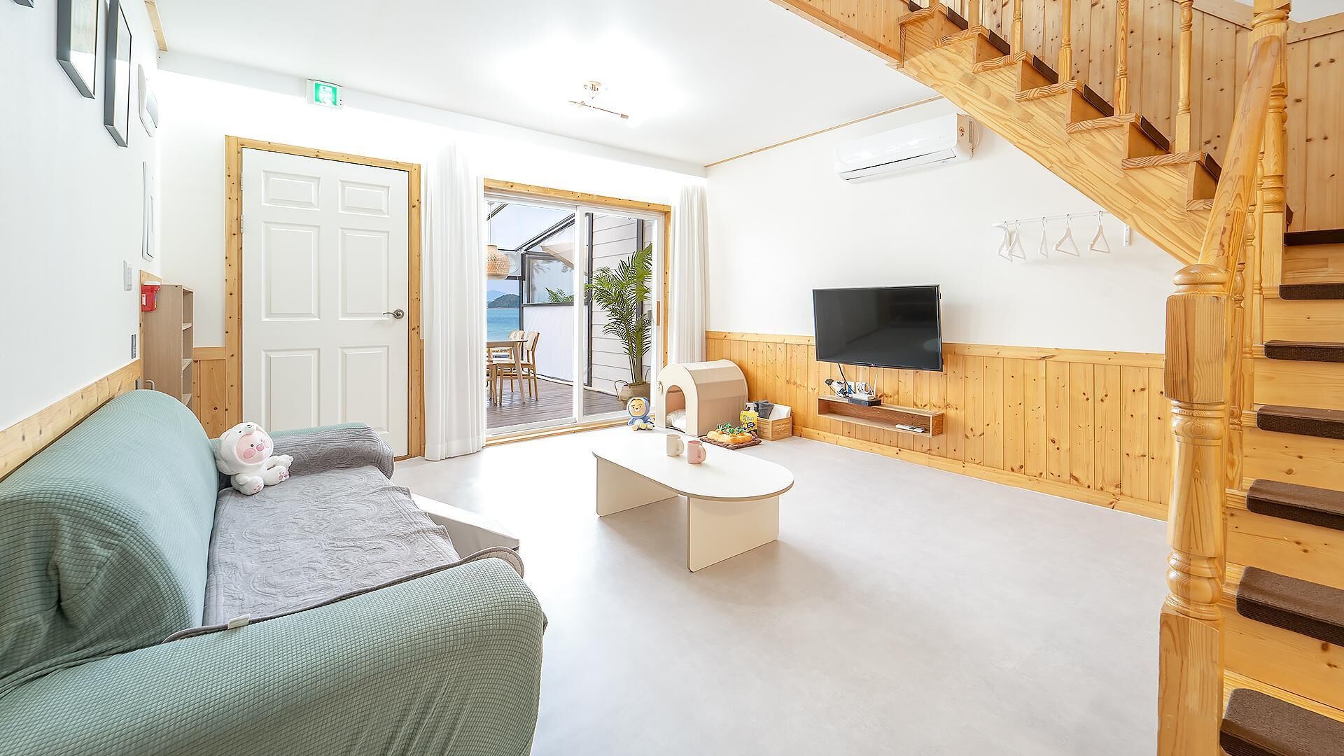 A hotel room with a wooden staircase, a sofa, a coffee table, a television, and a view of the outside.