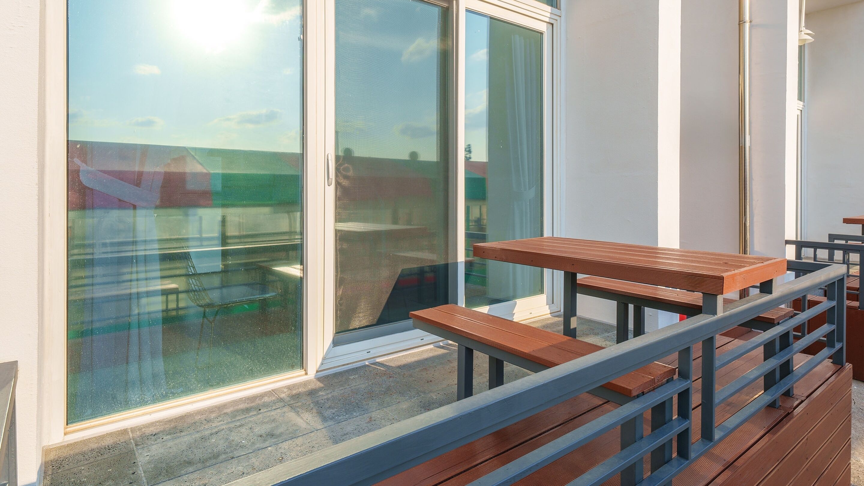A balcony with wooden tables and benches, a glass door, and a metal railing.