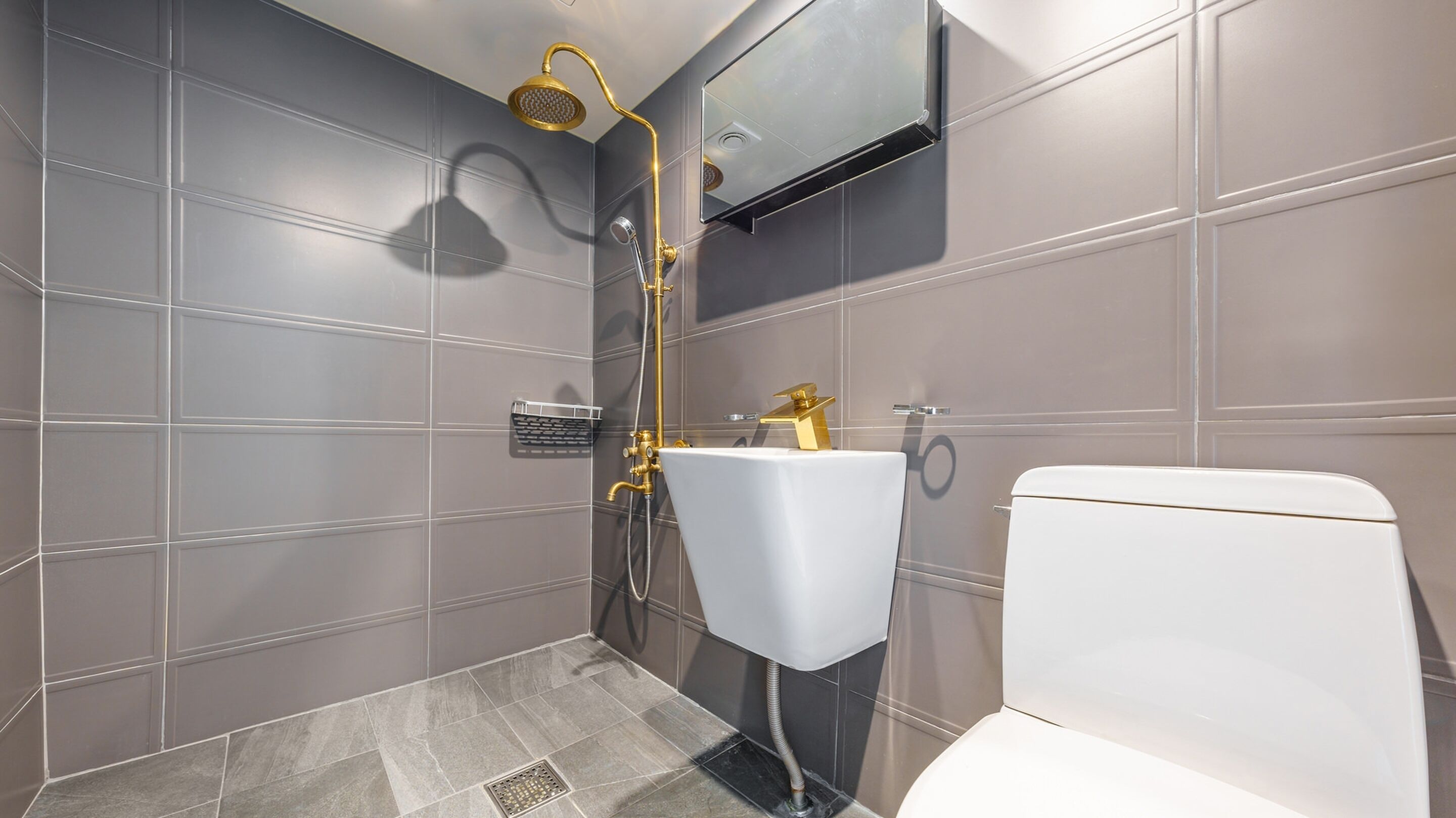 A modern bathroom with a white toilet, a gold showerhead, and a wall-mounted mirror.