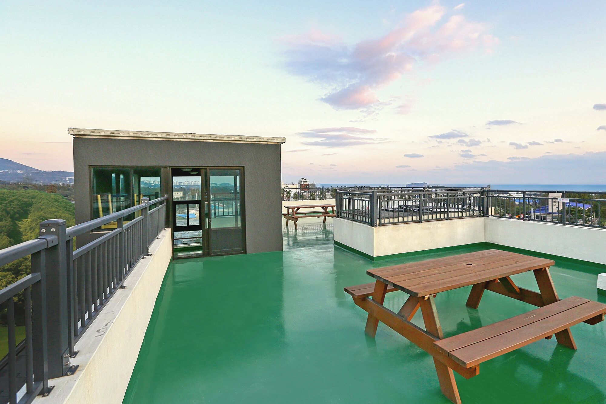 A rooftop terrace with a green floor, a wooden picnic table, and a glass door leading to an interior space.
