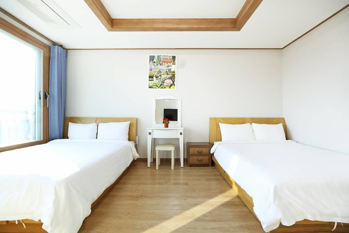 A hotel room with two beds, a desk, a chair, and a small table with a mirror.