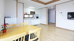 A modern kitchen with white cabinets, a built-in oven, and a microwave. There is a dining area with a wooden table and chairs, and a TV mounted on the wall.