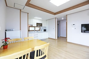 Een moderne keuken met witte kasten, een inbouwoven en een magnetron. Er is een eethoek met een houten tafel en stoelen, en een aan de muur bevestigde televisie.