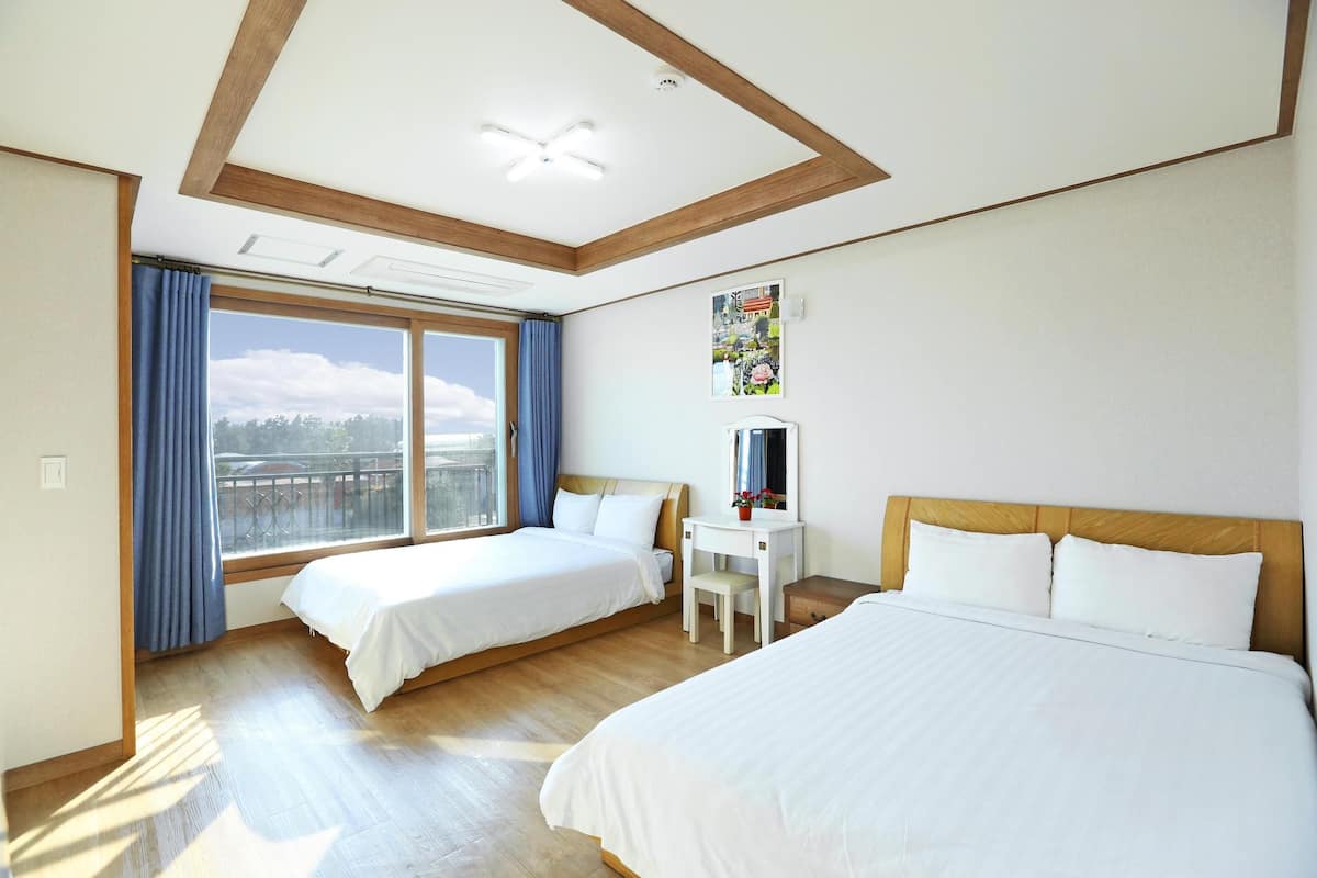 A hotel room with two beds, a desk, a chair, and a large window with curtains.