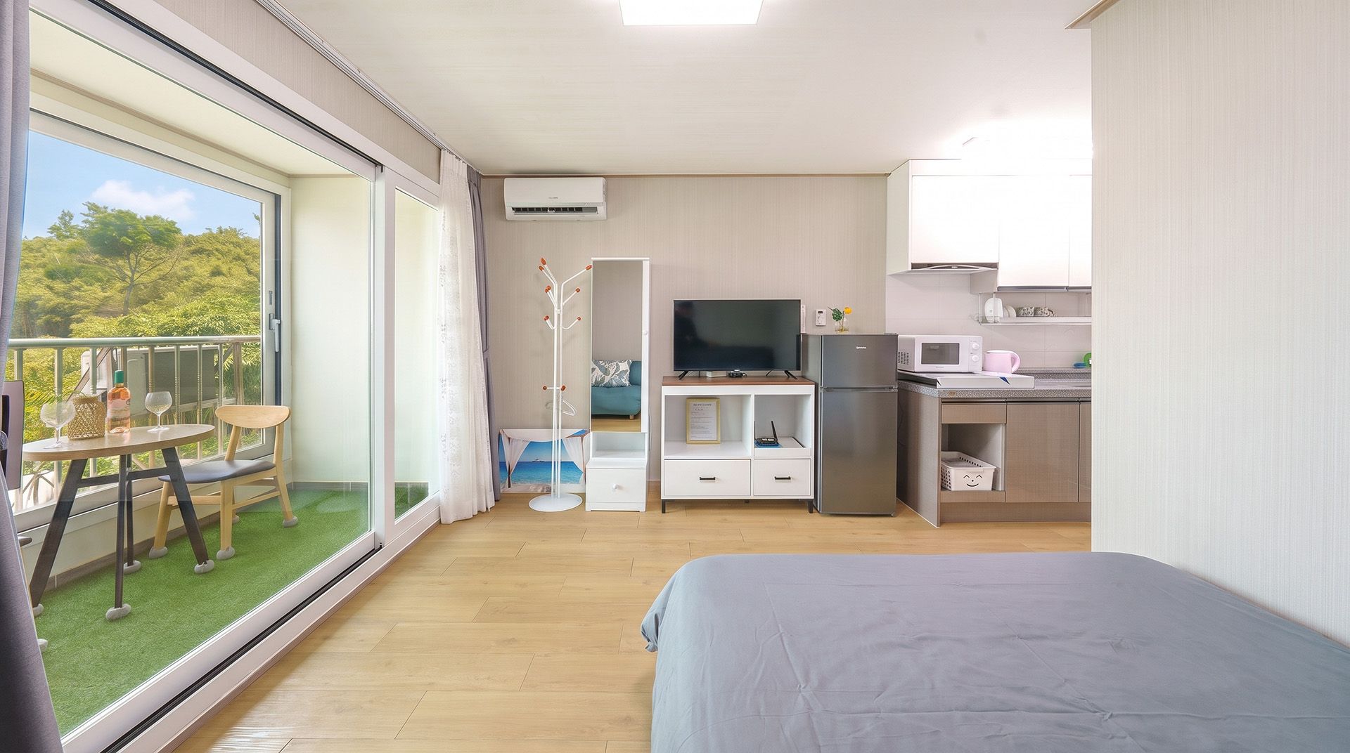 A modern room with a balcony, a bed, a TV, a fridge, and a kitchen area.