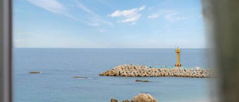 A coastal scene with a lighthouse on a breakwater, calm sea, and rocky outcrops.