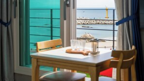 A table with chairs and a glass set, overlooking a rocky shoreline with a lighthouse. - Gangneung Glad Pension (Gangneung)