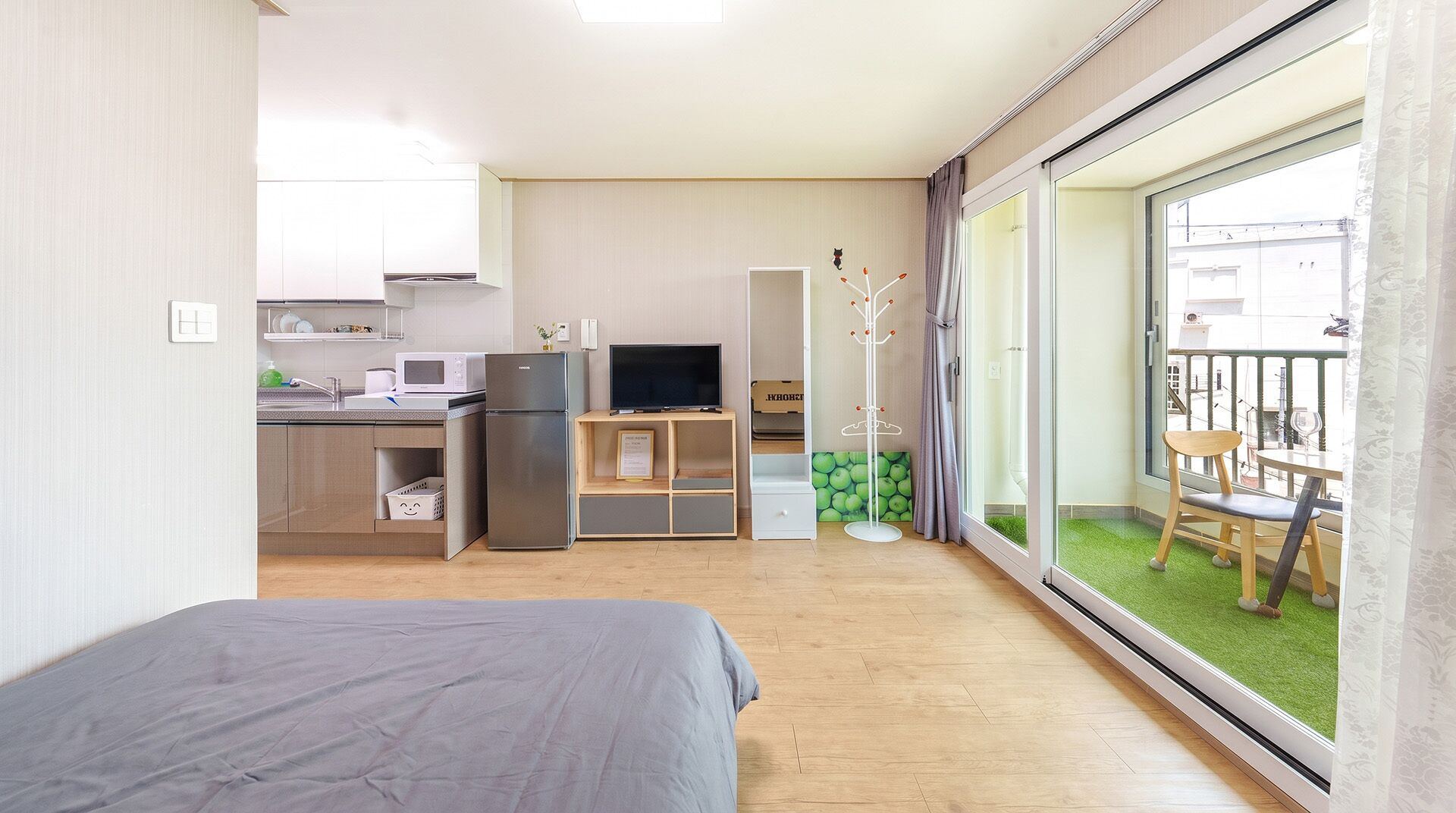 A compact hotel room with a bed, kitchenette, TV, and a balcony with a view.