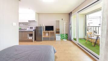 A compact hotel room with a bed, kitchenette, TV, and a balcony with a view.