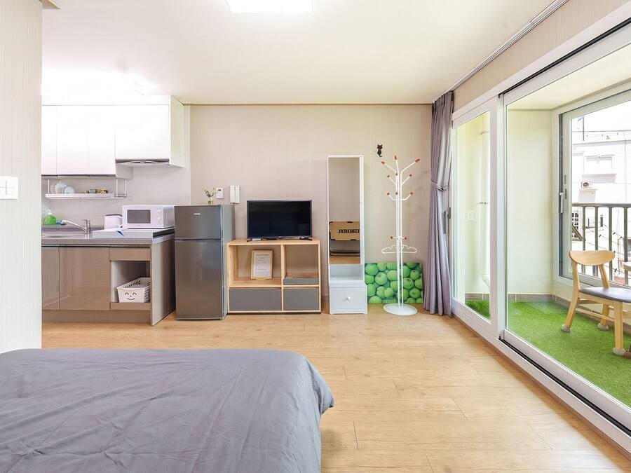 A compact hotel room with a bed, kitchenette, TV, and a balcony with a view.