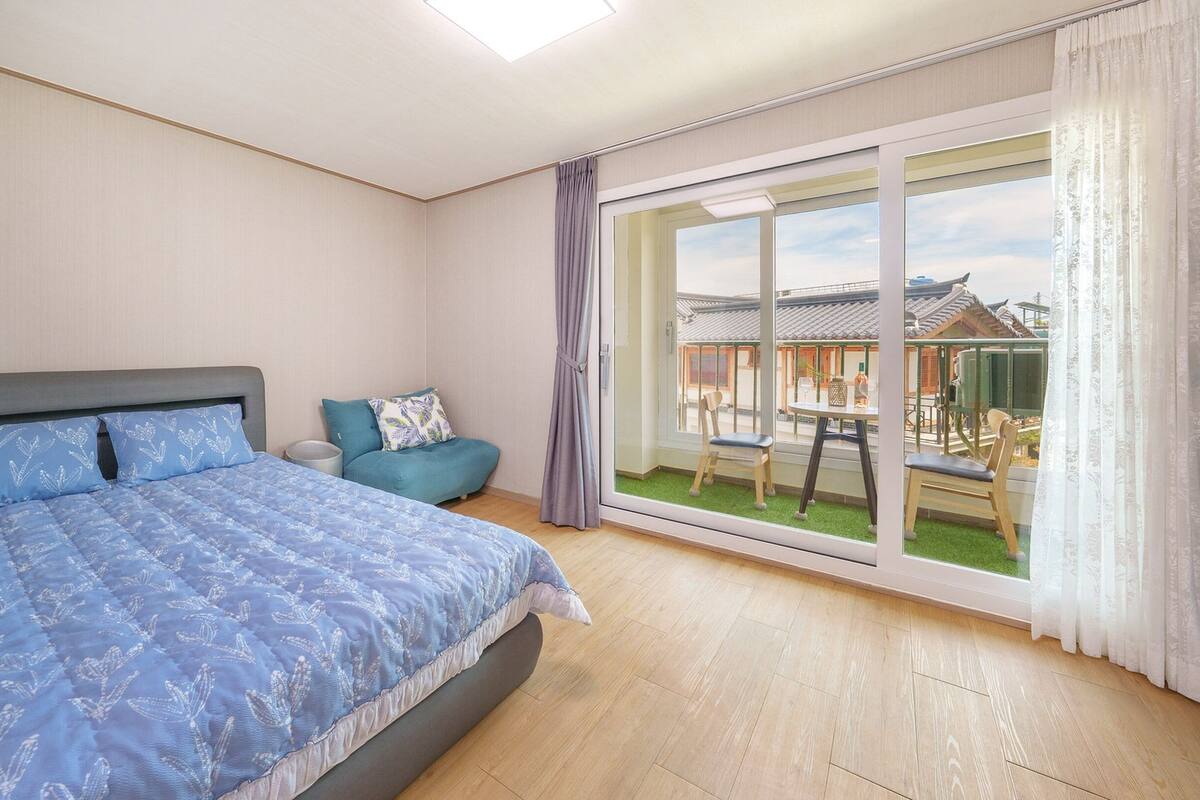 A bedroom with a bed, a chair, and a balcony with a view of traditional architecture.
