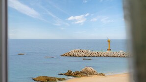 Paisaje costero con un faro en un rompeolas, mar tranquilo y playa arenosa.