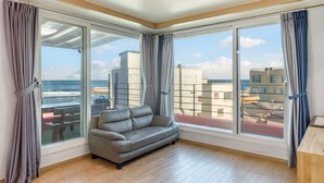Una sala de estar moderna con un sofá gris, ventanas amplias y vistas al mar y edificios.