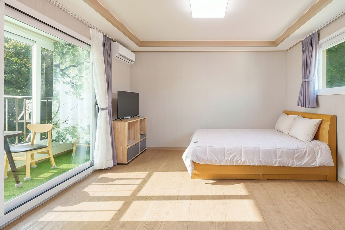 Een slaapkamer met een bed, een televisie op een houten standaard, en een balkon met een stoel en gordijnen.