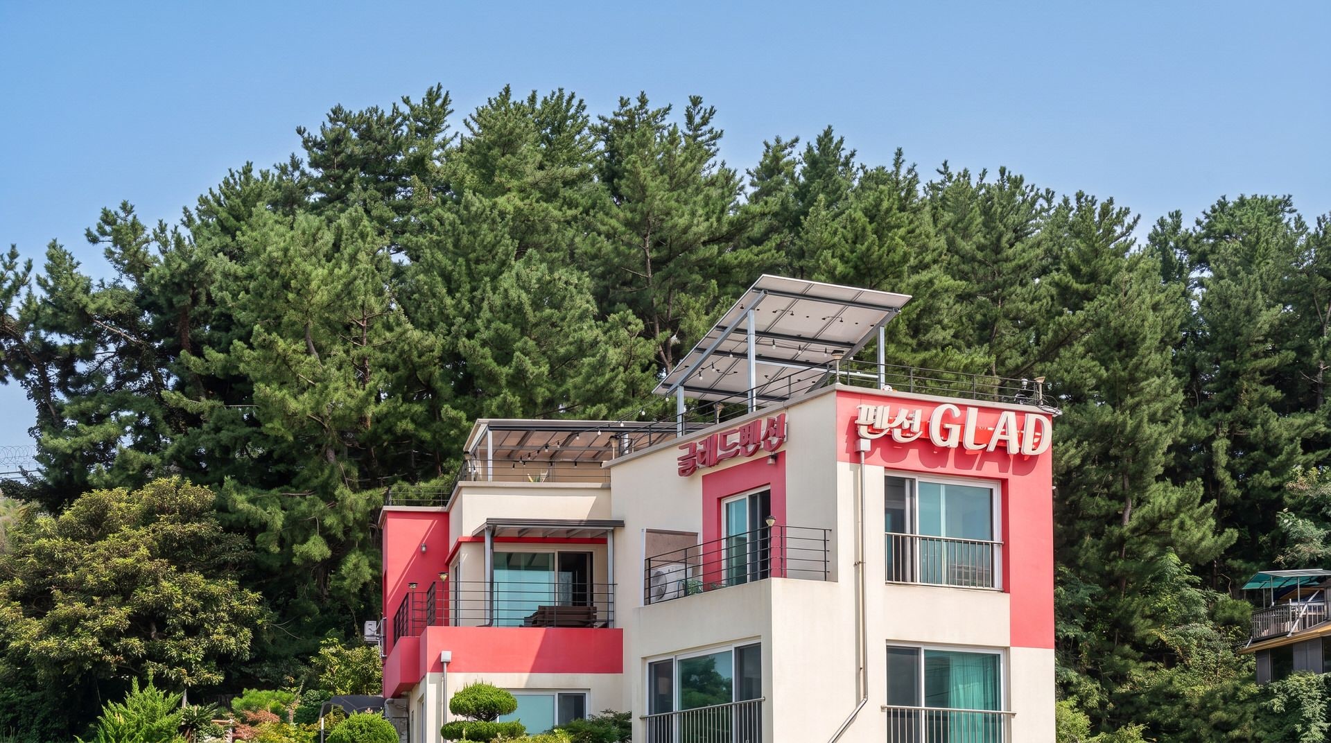 A modern building with a red and white facade, solar panels on the roof, and a sign that reads 'GLAD'.