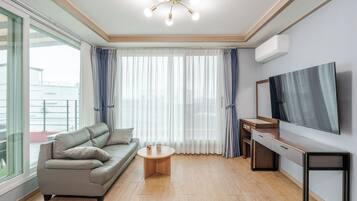 A modern living room with a sofa, a coffee table, a flat-screen TV, and a large window with curtains.