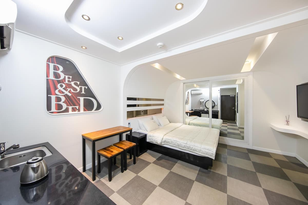 Une chambre d’hôtel moderne équipée d’un lit, d’un bureau, d’une petite table, d’un lavabo et d’un miroir.