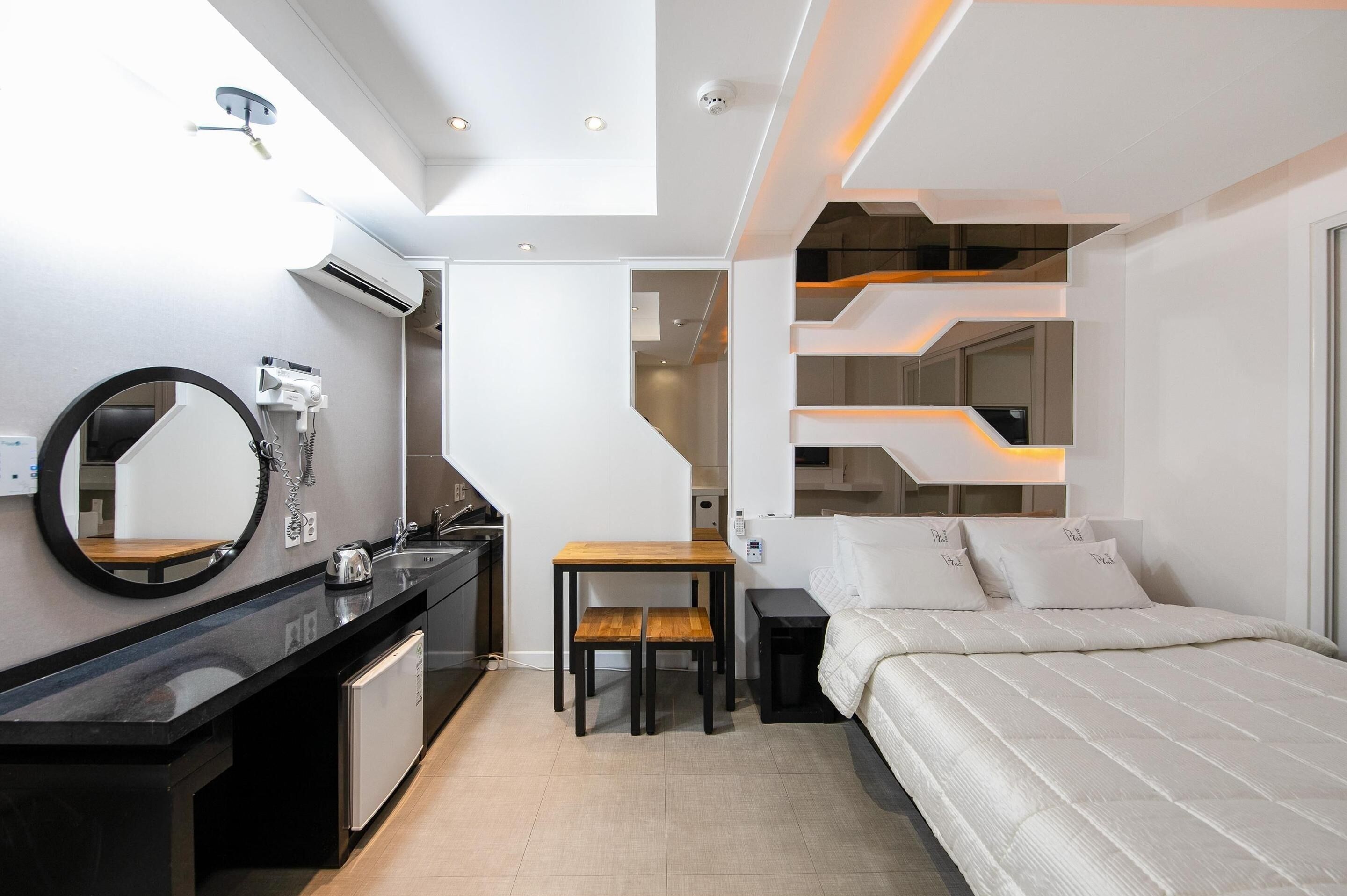 Una camera d'albergo moderna con un minibar nero, un tavolo da pranzo in legno, un letto con biancheria da letto bianca e un design di scala originale.