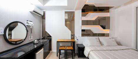 Una camera d'albergo moderna con un minibar nero, un tavolo da pranzo in legno, un letto con biancheria da letto bianca e un design di scala originale.