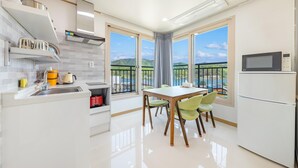 A modern kitchen with a dining area, large windows with a view of mountains, and a refrigerator. - Nami Island Pig Dream Spa Pension (Gapyeong)