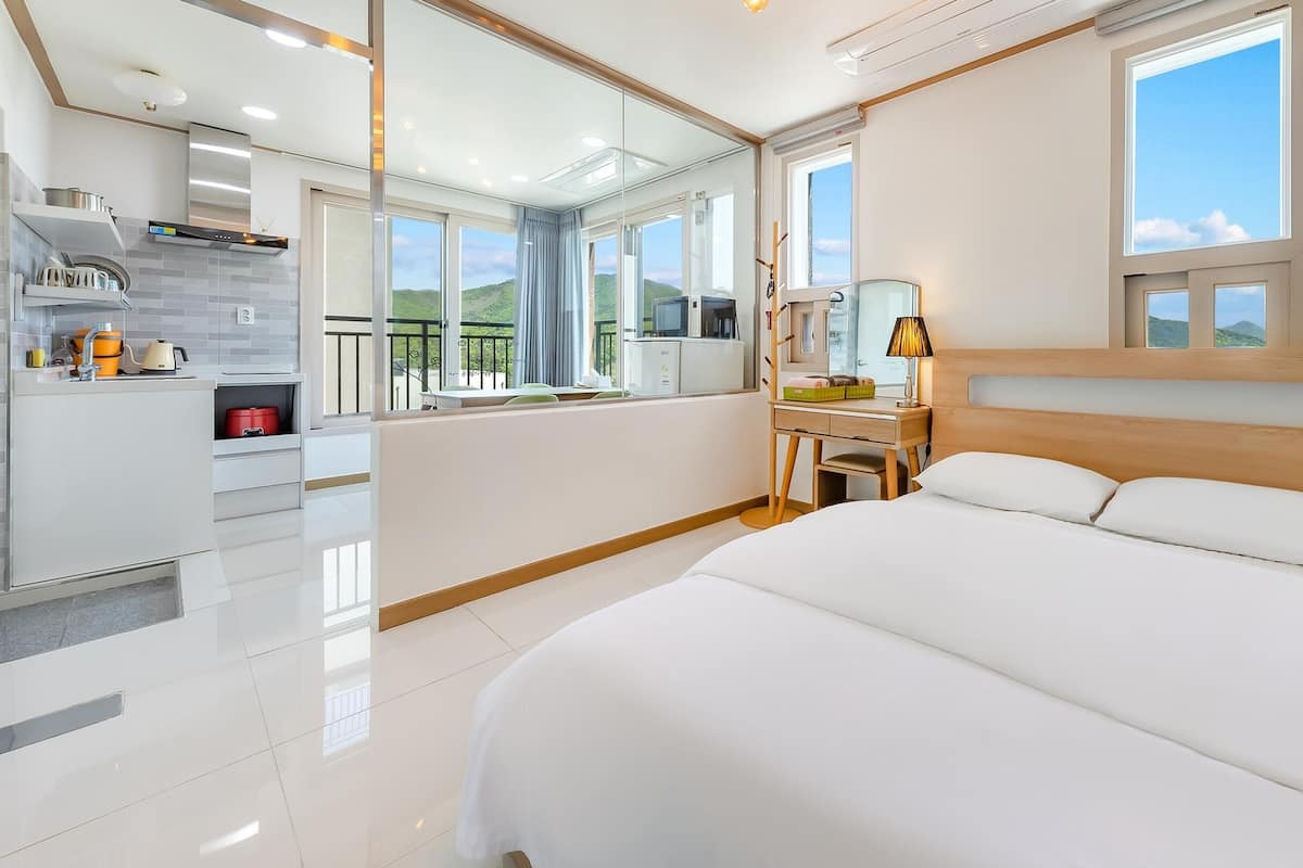 A modern hotel room with a large bed, a desk, a mirror, and a view of the outdoors.