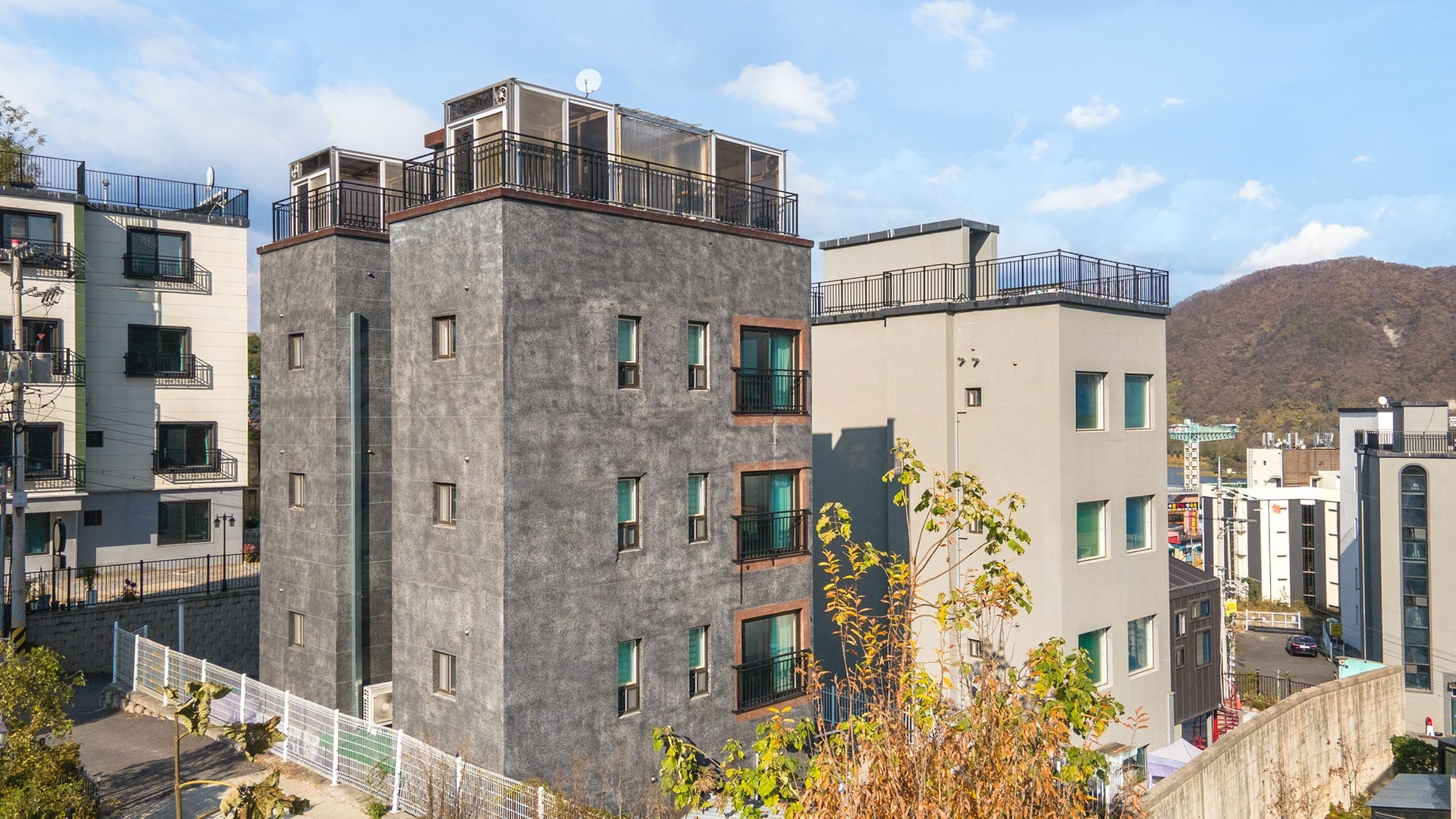 A modern apartment building with multiple balconies, large windows, and a view of a hilly landscape.